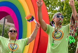 TD colleagues in green t-shirts and rainbow face paint hand out Pride flags and whistles on a TD float in a Pride parade.