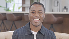 Brandon Gonez smiles while seated on a beige leather couch. 