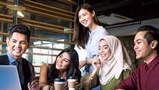 A diverse group of TD colleagues share smiles while seated around a laptop for a video conference.