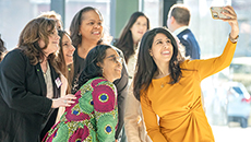 A group of women from diverse cultural backgrounds pose for a selfie while attending a conference.