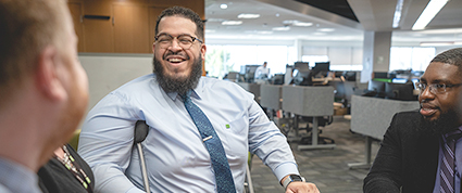 A racially diverse group of TD colleagues including a man that uses crutches conduct a meeting in an office.