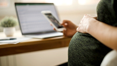 A pregnant TD colleague in a green dress checks her phone while resting her hand on her belly.