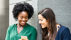 Two racially diverse TD colleagues stand outside their office looking at their phones. 