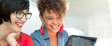Two female entrepreneurs seated in front of a laptop smile while reading an email.