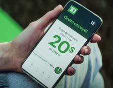 Une main tient un téléphone, sur lequel est affichée l’appli TD